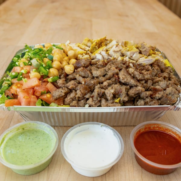 Halal Bros combo platter with chicken, lamb, chickpeas, salad, and three sauces on a wooden table.
