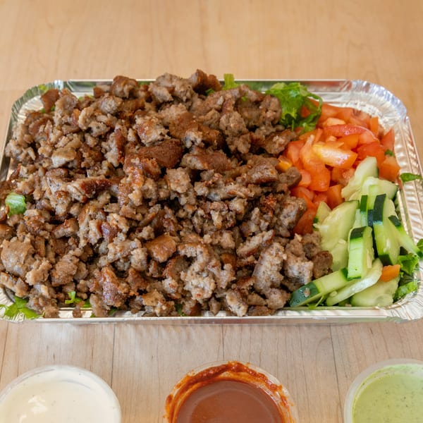Halal Bros' chopped halal meat platter with diced tomatoes, cucumbers, and lettuce, with three sauces.