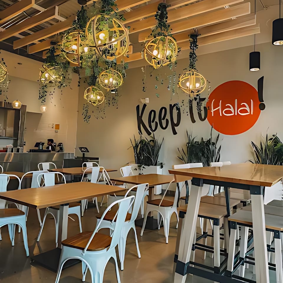 Halal Bros restaurant interior with tables, chairs, and a wall mural that reads "Keep it Halal!"