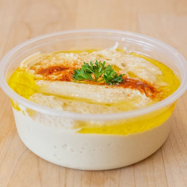 Halal Bros hummus in a clear plastic container, topped with olive oil, paprika, and parsley.