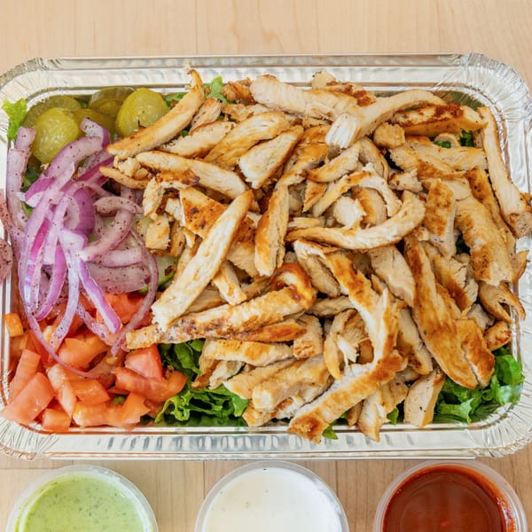 Halal Bros chicken platter with lettuce, tomatoes, red onions, pickles, and three sauces.