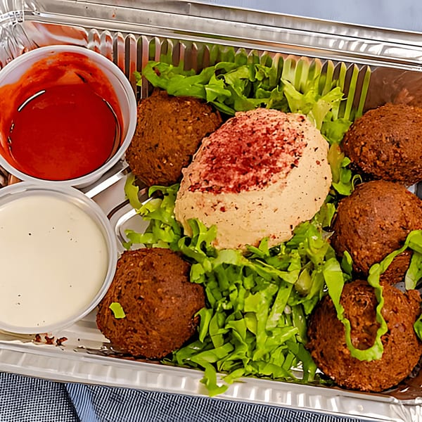 Halal Bros falafel platter with hummus, lettuce, red sauce, and white sauce in a foil container.