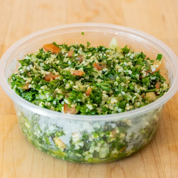 Halal Bros' tabbouleh salad, a vibrant mix of parsley, tomatoes, and bulgur, in a clear plastic container.
