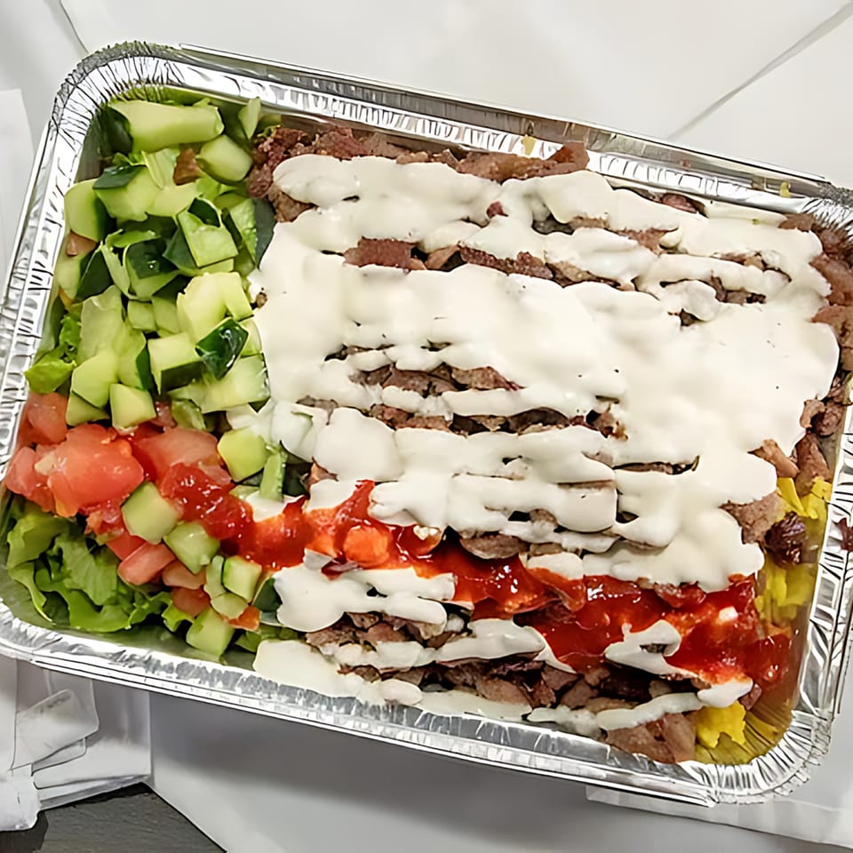 Halal Bros' large platter of halal meat, rice, salad, white sauce, and red sauce in a foil container.