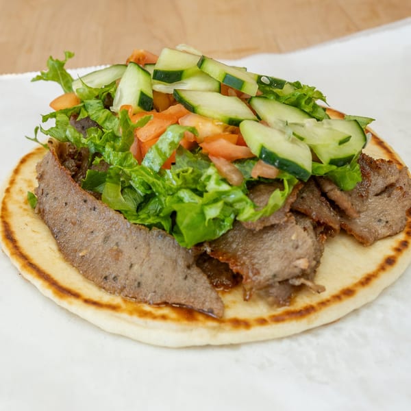 Halal Bros gyro with sliced meat, lettuce, diced tomatoes, and cucumbers on pita bread.