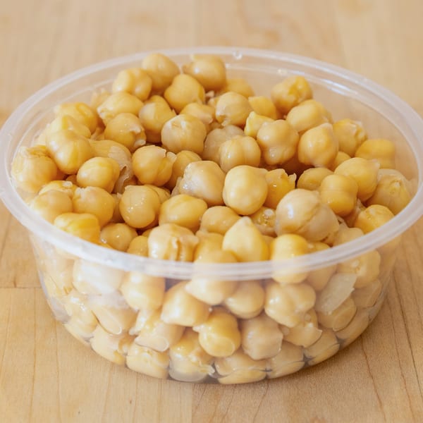 A clear plastic container filled with cooked chickpeas sits on a light wooden surface.