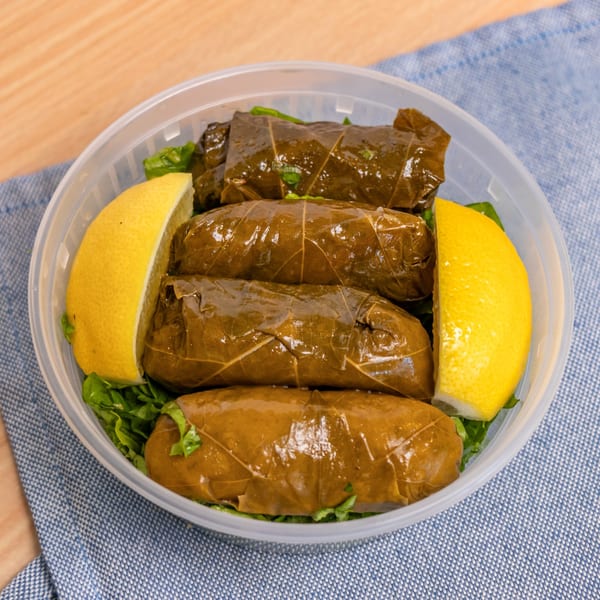 Halal Bros' dolmas, grape leaves stuffed with rice, served with lemon wedges in a plastic container.