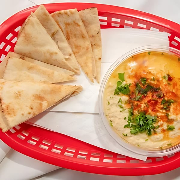 Halal Bros hummus with parsley and paprika, served with pita bread in a red basket.