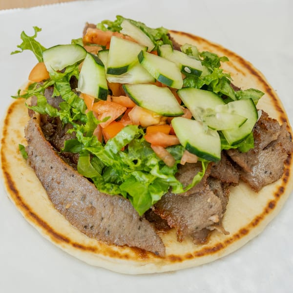 Halal Bros gyro with sliced meat, lettuce, diced tomatoes, and cucumbers on pita bread.