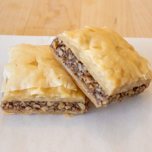 Two pieces of golden-brown baklava with a rich nut filling, on a white surface.