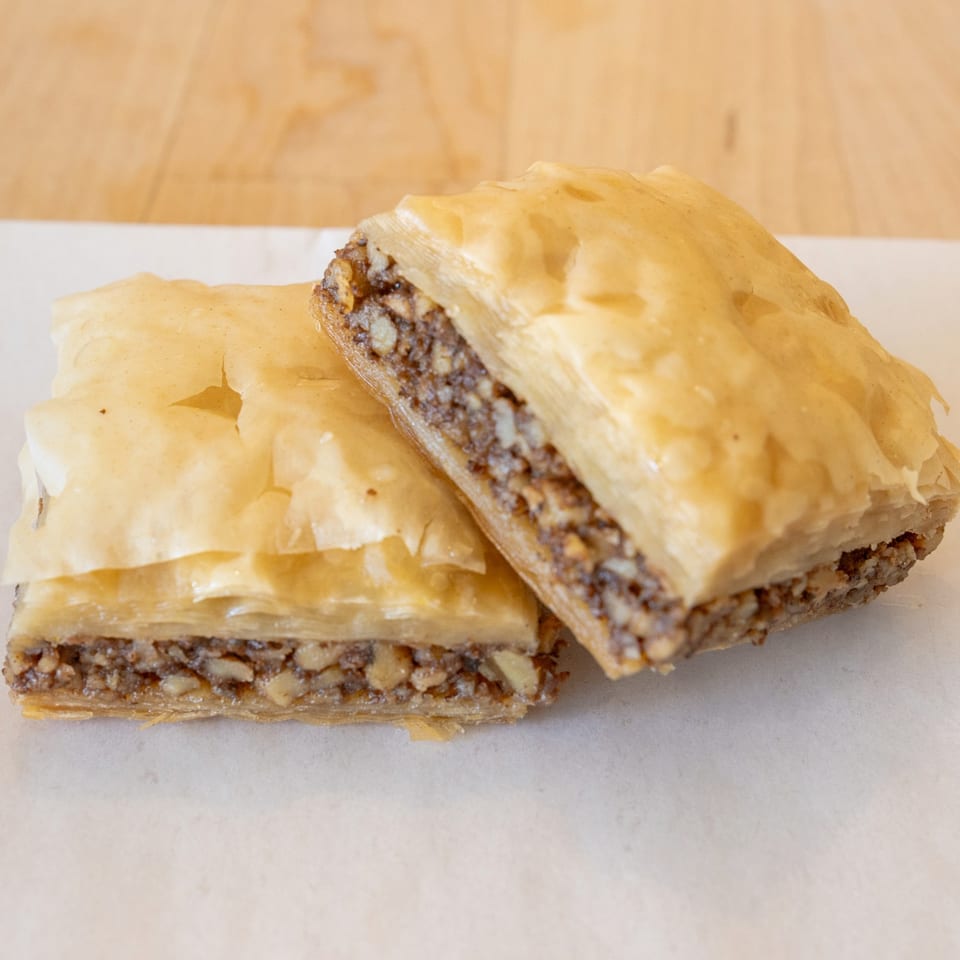 Two pieces of golden-brown baklava with a rich nut filling, on a white surface.