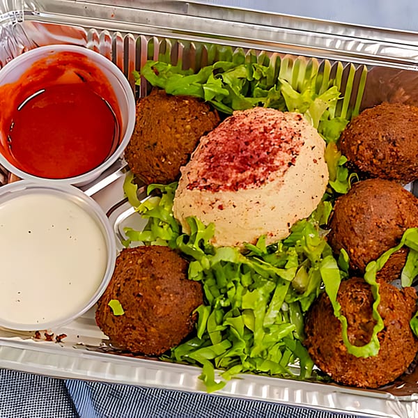 Halal Bros falafel platter with hummus, lettuce, red sauce, and white sauce in a foil container.