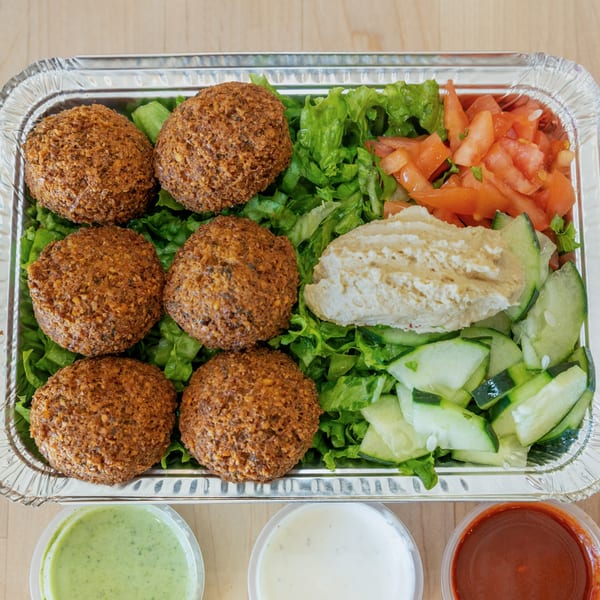 Halal Bros falafel platter with six falafel, salad, hummus, and three sauces in a foil container.
