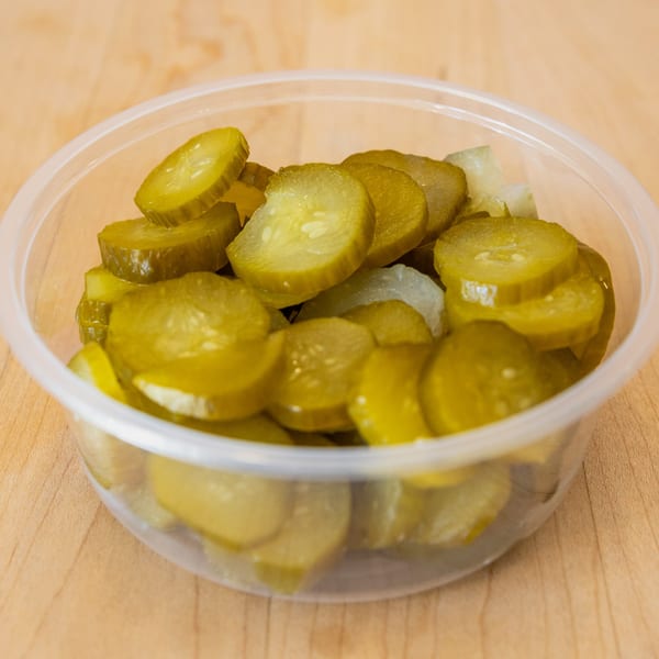 A clear plastic container filled with sliced dill pickles and some chopped white onions.