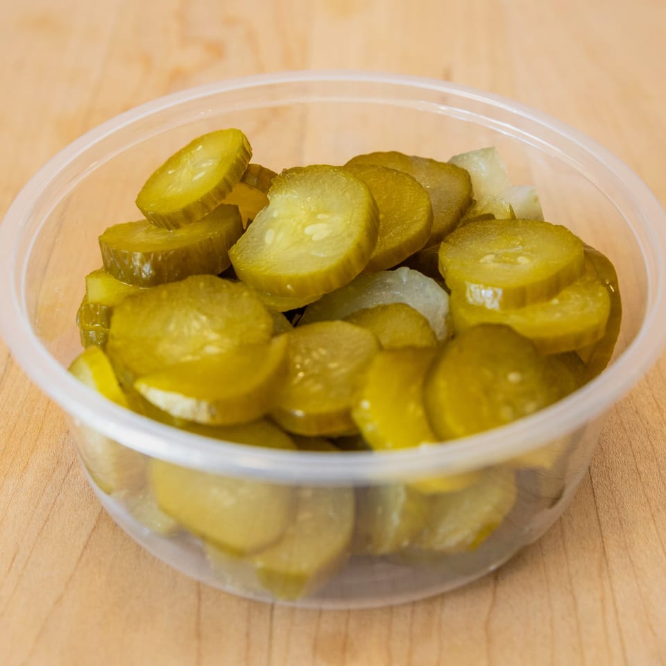 A clear plastic container filled with sliced dill pickles and some chopped white onions.